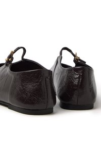 Dark brown leather shoes with a textured finish, featuring a small ankle strap and gold buckle accents. Flat soles and rounded backs.