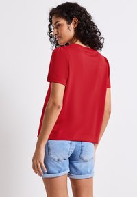 Top corto rosso a maniche corte in tessuto morbido, con una vestibilità rilassata e scollo rotondo, abbinato a pantaloni corti di denim blu chiaro con orli arrotolati.