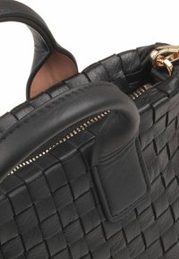 Sac à main en cuir noir avec un design tissé, des poignées arrondies et une fermeture éclair dorée avec une tirette. Détail de surface texturé visible.