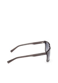 Gafas de sol polarizadas con lentes gris oscuro, montura de plástico marrón mate y patillas texturizadas. Presenta el logo de Timberland en la montura.