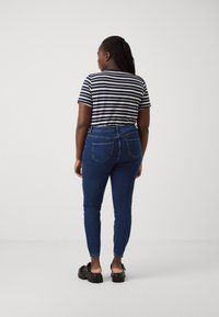 Jeans ajustados azules con una cintura alta, combinados con una camiseta de rayas blancas y negras. El modelo lleva sandalias negras con suelas gruesas.