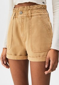 Beige Jeans-Shorts mit einem gerafften elastischen Bund, einer Vorderknopf-Leiste, umgeschlagenen Säumen und zwei vorderen Taschen, die eine glatte Textur zeigen.