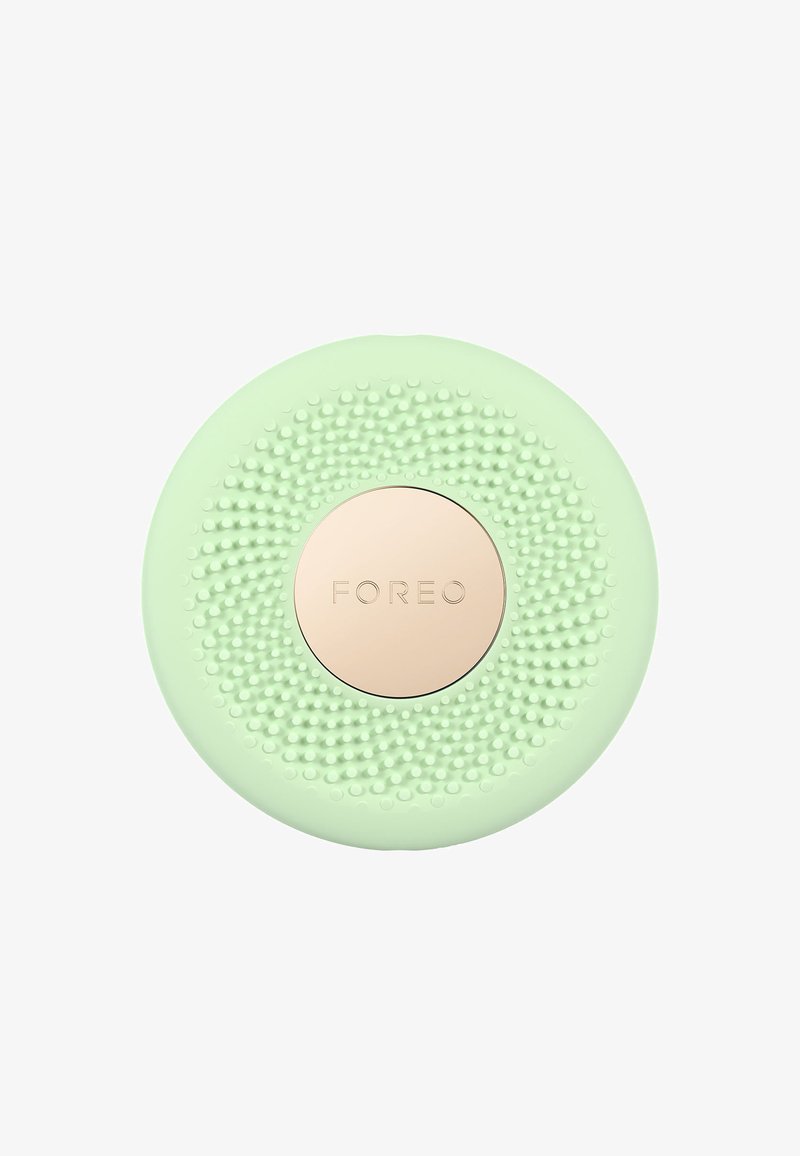 Round, mint green facial cleansing device with textured silicone surface and a rose gold center embossed with "FOREO."