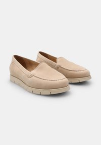 Beige slīdējošās kurpes, izgatavotas no mīksta zamša, ar noapaļotu purngalu, dūriena detaļām un klinšu zoli ar mazām izgriezumiem, lai nodrošinātu saķeri.