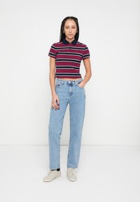 Polokošeľa s krátkym rukávom v bordových a námorníckych pruhovaných farbách, doplnená o svetlomodré rifle s rovnými nohavicami. Obuv tvoria béžové tenisky.