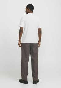 T-shirt polo blanc à manches courtes, en tissu texturé, col côtelé et poignets contrastés ; associé à un pantalon large marron foncé et des chaussures noires.
