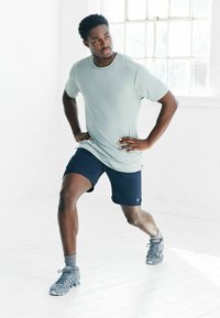 Hellgraues sportliches T-Shirt und dunkelblaue Shorts mit entspannter Passform. Graue Laufschuhe mit Netztextur und Gummisohlen.