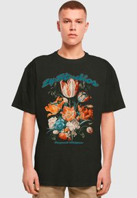 Svart bomulls t-skjorte med blomsterdesign i oransje, blått og hvitt. Tekst "Fragant Whispers" i turkis over blomstene.