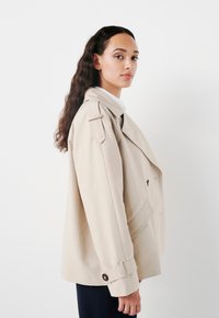 Giacca beige con design doppiopetto, vestibilità oversized, spalline e polsini con bottoni. Texture liscia e dettagli minimi.