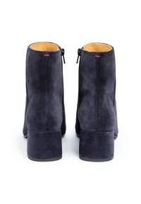Botas de ante azul marino hasta el tobillo con un tacón bloque, que cuentan con cremalleras laterales y un forro interior suave. Detalladas con un pequeño hilo rojo.