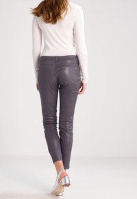 Pantalones ajustados grises con una textura lisa y brillante; bolsillos en la parte trasera; combinados con una blusa blanca de manga larga y zapatos de tacón plateados.