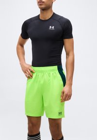 Αθλητικό άτομο που φοράει μαύρο στενό μπλουζάκι Under Armour και φωτεινά πράσινα αθλητικά σορτς με μαύρες και πράσινες πλαϊνές λεπτομέρειες.