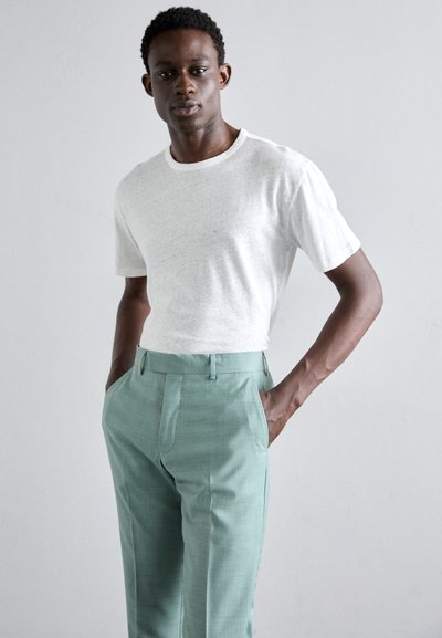 T-shirt branca texturizada combinada com calças tailored verdes claras, apresentando frente lisa e bolsos laterais. Design simples e contemporâneo.