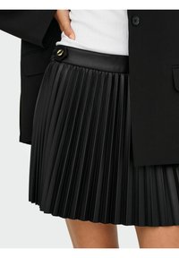 Must nagu plisseeritud seelik, mis on valmistatud kunstnahast, millel on sile vöökoht koos kuldsete detailidega. Plisseeringud loovad struktureeritud ja tekstuurilise välimuse.