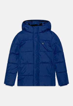 Giacca puffa blu con cappuccio e design trapuntato, chiusura frontale con zipper, polsini elastici e dettaglio del logo sul lato sinistro del petto. Texture liscia.
