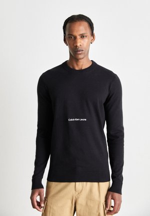 Suéter negro de tejido de punto, con cuello redondo y puños acanalados. Texto del logo en blanco "Calvin Klein Jeans" centrado en la parte frontal.