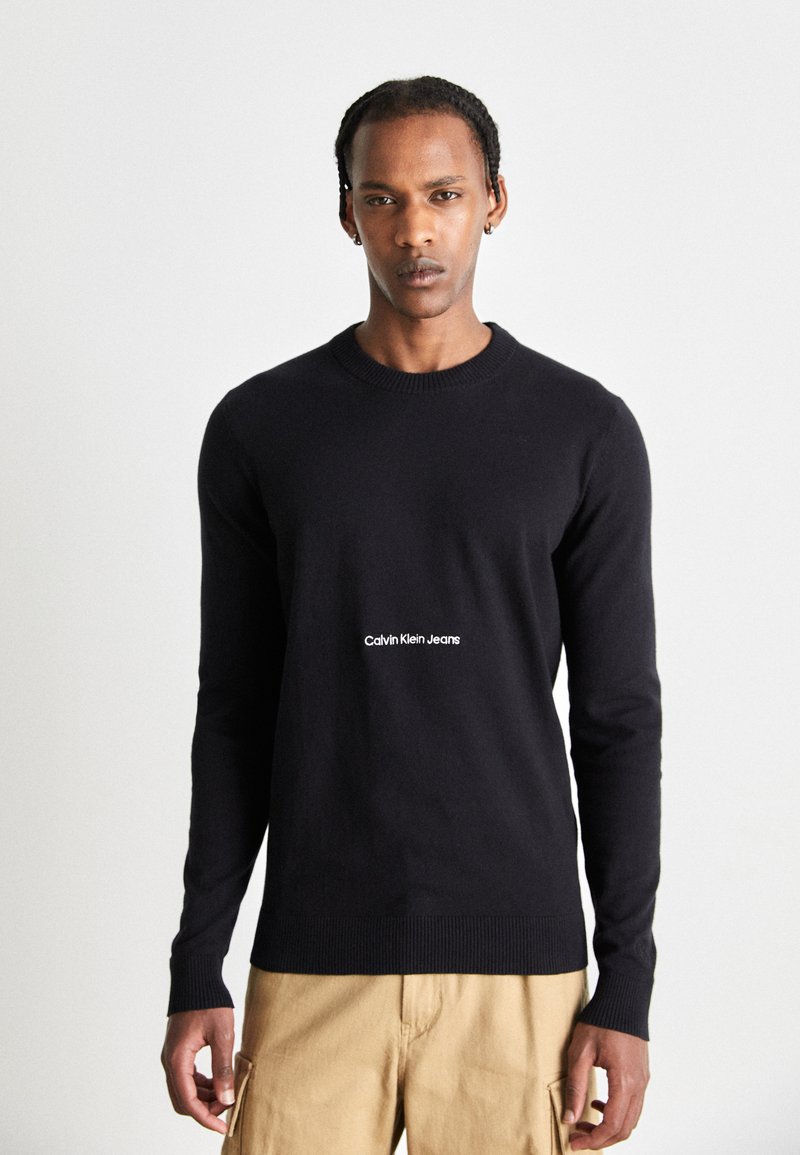 Maglione nero realizzato in tessuto lavorato a maglia, con scollatura a girocollo e polsini a coste. Testo del logo bianco "Calvin Klein Jeans" centrato sul davanti.