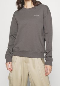 Mörkgrå sweatshirt i en bomullsblandning med ribbade muddar och nederkant, med en liten vit "NA-KD"-logotyp på bröstet.
