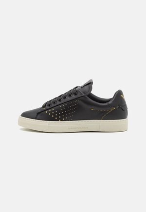 Baskets en cuir noir avec un motif d'étoiles dorées, bout rond, semelle plate beige et design à six œillets. Logo de la marque sur le talon et sur le côté.