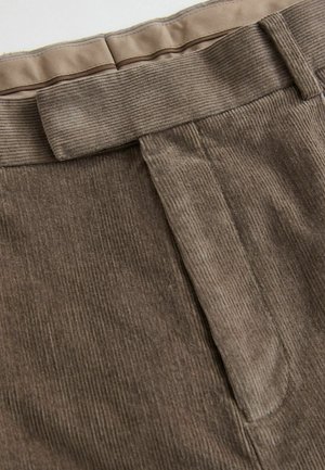 Brown corduroy fabric with vertical ridges, featuring a smooth waistband and a clean front design. Minimalist stitching and accents visible.