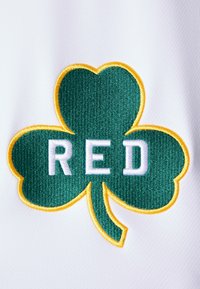 Haft zielonego koniczynki z żółtą obwódką i słowem "RED" w białym tekście, umieszczony na białym tle z tkaniny.