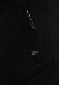 Mustast kangast tasku musta tõmblukuga, millel on valgekirjud tõmbenöörid ja väike must silt, millel on kiri "BIG STAR".