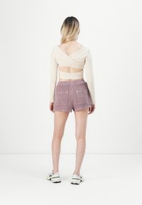 Haut beige à manches longues enroulé avec une découpe dans le dos, associé à un short texturé violet clair avec deux poches latérales.