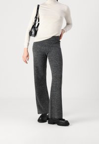 Grå utsvängda byxor i texturerat tyg, ihop med en ljusbeige polotröja. Accessoarerna inkluderar en liten svart handväska. Svarta klumpiga skor.