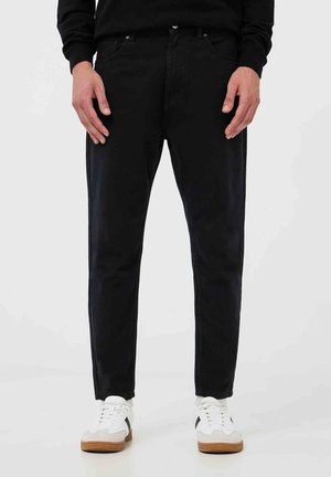 Svarta denimjeans med en slim fit-design. Har bälteshällor, framfickor och en subtil textur. Kombineras med vita sneakers och en svart topp.