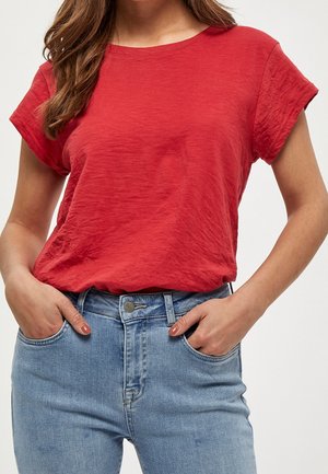 Red short-sleeve t-shirt with a relaxed fit and round neckline, paired with light blue high-waisted jeans featuring front pockets.