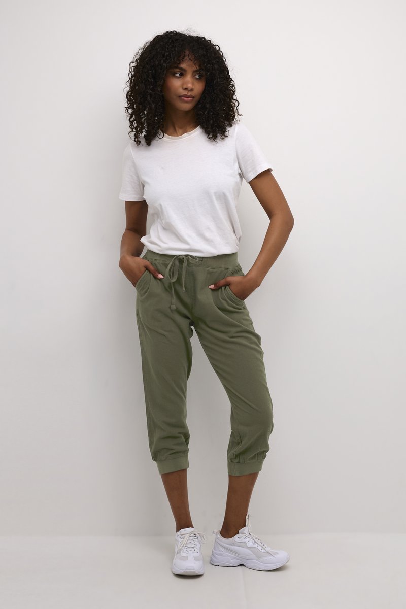 T-shirt blanc léger associé à un jogger court olive avec une taille élastique et deux poches latérales, porté avec des baskets blanches.