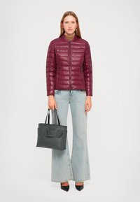 Giacca a vento bordeaux con un design aderente, abbinata a jeans flare in denim chiaro. Tieni una borsa nera strutturata con doppio manico.