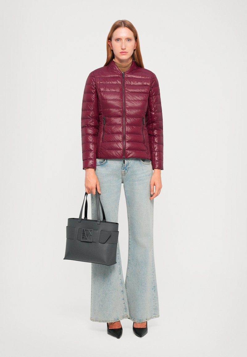 Giacca a vento bordeaux con un design aderente, abbinata a jeans flare in denim chiaro. Tieni una borsa nera strutturata con doppio manico.
