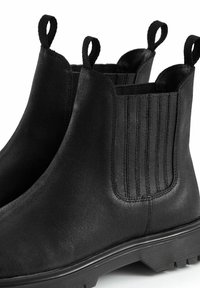 Botas Chelsea negras de cuero suave con paneles elásticos en los lados y tiradores, que cuentan con una suela de goma texturizada y detalles cosidos.