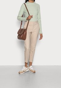 Maglietta a maniche lunghe a righe verde chiaro, pantaloni beige su misura, borsa a tracolla marrone e sneakers beige con dettagli bianchi.
