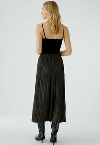 Zwarte geplooide maxi-jurk met een elastische tailleband, gecombineerd met een aansluitend zwart hemd. Lichte textuur en vloeiende ontwerp voor gemakkelijke beweging.