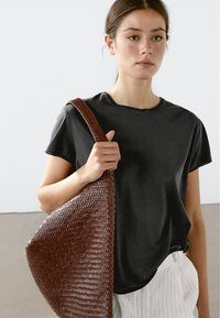 Sort T-shirt med korte ærmer, parret med en stor, vævet brun håndtaske. Tasken har et tekstureret, slasket design.