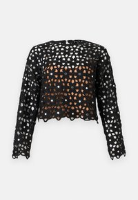 Haut long à manches longues en crochet noir avec motif floral et petites garnitures de miroirs ronds sur un fond clair uni.