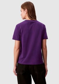 Fioletowy bawełniany t-shirt z krótkimi rękawami, okrągłym dekoltem i gładką fakturą. Widok od tyłu pokazuje prosty design bez ozdób i wzorów.