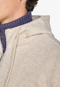 Lys grå fleece zip-up jakke med hætte, der har et struktureret stof, kontrasterende ribbet marineblå krave og elfenbensfarvede snore.
