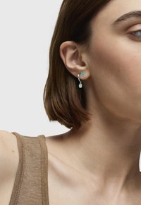 Pendientes de aro plateados con detalles de oso de turquesa y colgantes; los pendientes se muestran en un modelo con un corte bob corto.
