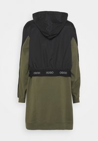 Veste à capuche avec une partie supérieure noire et un tissu vert olive en dessous, dotée d'une ceinture élastique et d'un détail de marque. Manches longues, design décontracté.