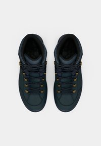 Mittelhohe Stiefel mit einem dunkelgrünen Lederobermaterial, strukturierten marineblauen Akzenten, goldenen Ösen und gemusterten Schnürsenkeln. Gummisohlen für guten Halt.