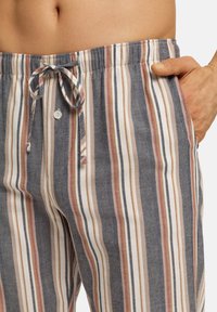 Raikkaat lounge-housut sinisissä, valkoisissa ja beigen raidallisissa väreissä, joissa on naruvyötärö, napin sulku ja sivutaskut, pehmeä tekstuuri.