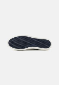 Bijela potplata tenisica s teksturiranim gumenim uzorkom. Plavi unutarnji dio ima male okrugle izbočine. Logotip "Levi's" utisnut je na strani.