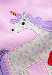 Appliqué unicorn design with a purple mane and orange horn, set on a light pink background, featuring blue polka dots and red accents.