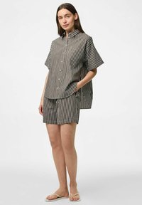 Randig kortärmad skjorta och shorts-set i svart och vitt. Har knäppning framtill, lös passform och fickor på skjortan. Platta sandaler används.