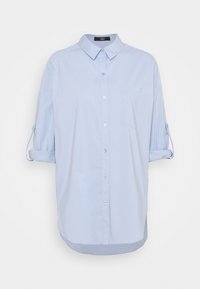 Chemise bleu clair à manches longues avec boutons, manches retroussées et col pointu sur fond blanc uni.
