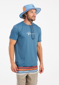 Blaues kurzärmliges Hemd mit strukturiertem Stoff und weißem Logo, kombiniert mit mehrfarbigen gestreiften Shorts und einem blau-orangen Bucket Hat.