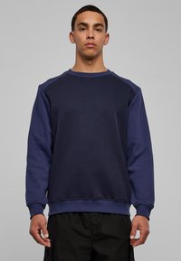 Marineblauwe sweatshirt met een ronde hals en raglanmouwen. Gemaakt van zacht stof, met een effen voorkant en textuurrijke accentuering op de mouwen.